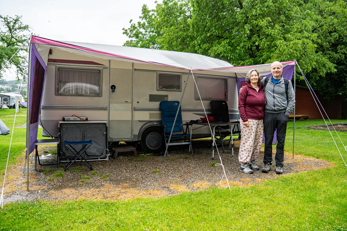 Ein Paar steht bei schlechtem Wetter vor einem Campingwagen.